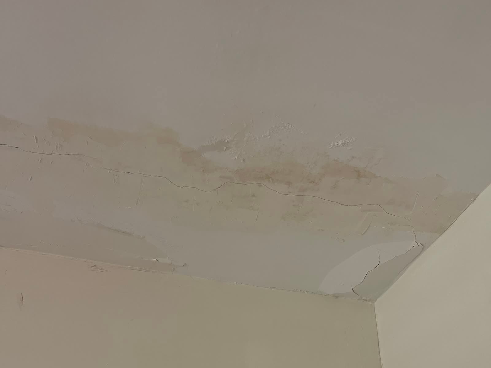 תקרה עם כתמי רטיבות חומים, טיח מתנפח וסדק ארוך לאורך המפגש עם הקיר